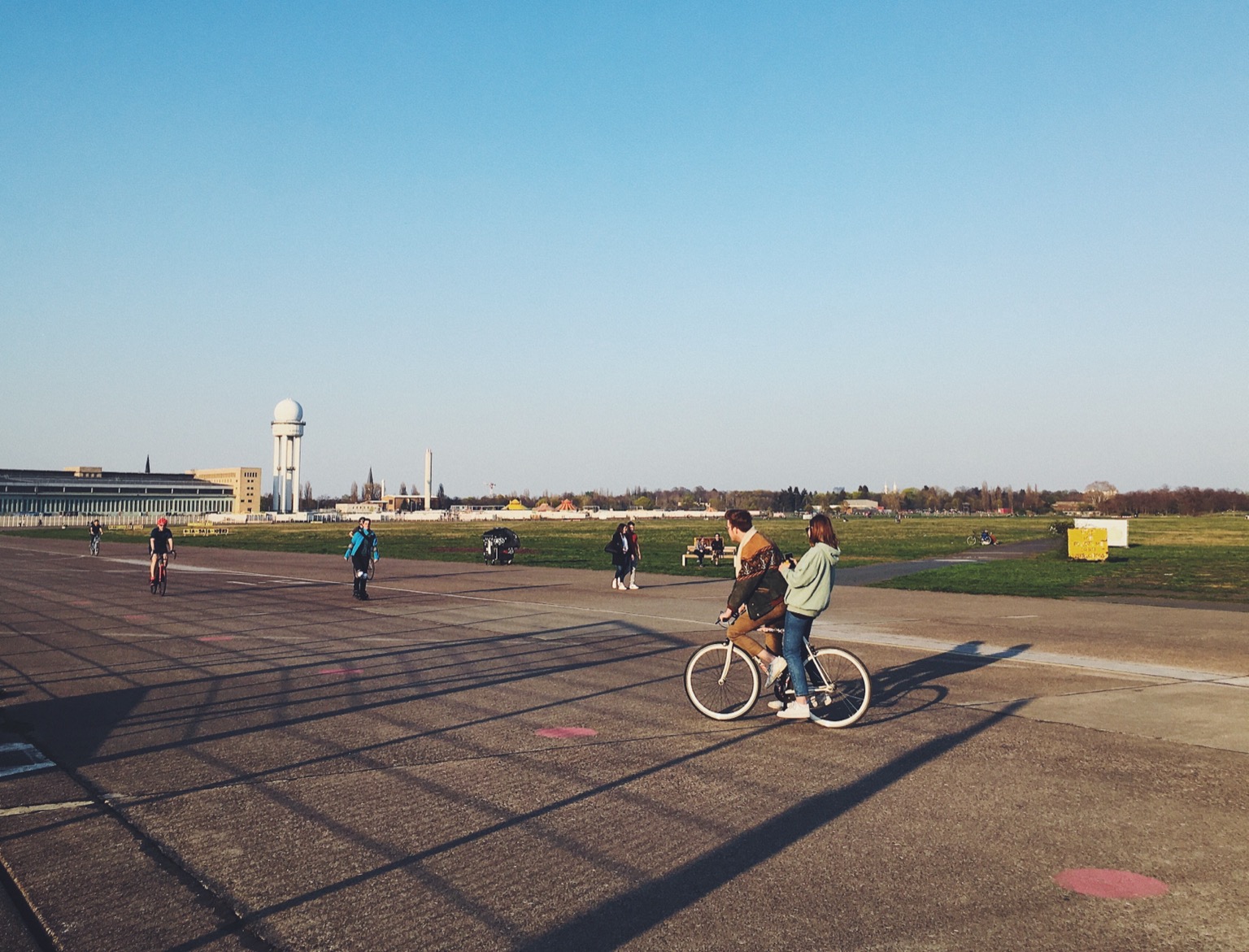 Two people riding a single bike on the old tarmac of Tempelhof Park in Berlin.