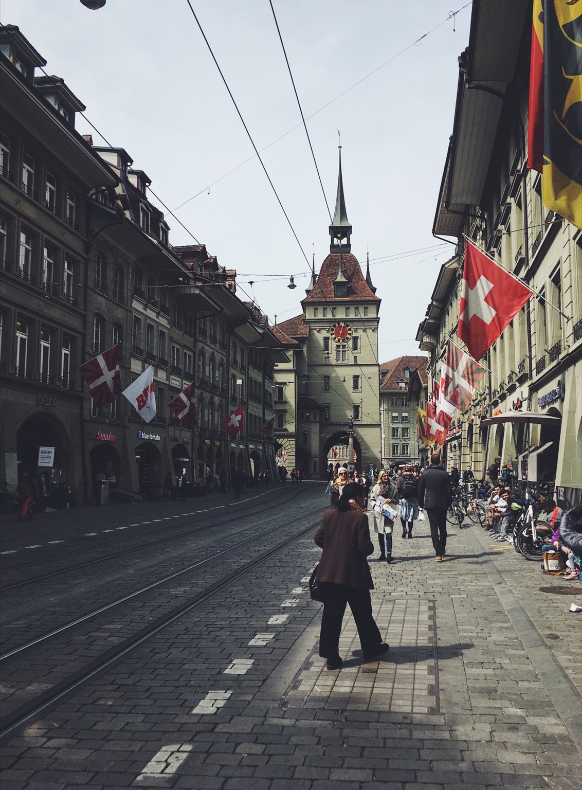 A street full of people walking in Bern, Switzerland with Swiss flags at every door.